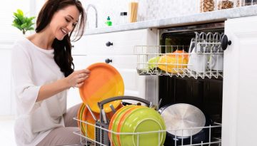 Smiling Young Woman Arranging Plates In Dishwasher At Home